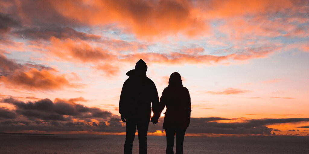 couple main dans la main admirant un coucher de soleil